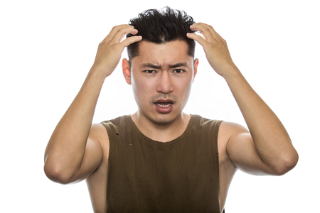 Athletic Asian male with trendy torn sleeveless shirt on a white background.  He is displaying failure expressions or gestures.  The handsome chinese or japanese man is muscular and physically fitの写真素材