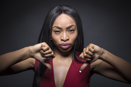 Black female model on a dark background with disapproval expressions.  She has her thumbs down.の写真素材