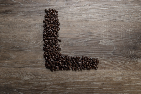 Dark roasted coffee bean arranged on a wooden table in the shape of text alphabet letter Lの写真素材