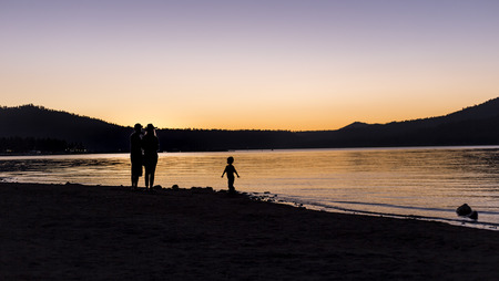 Silhouette of parents with a child watching the sunset over a lake.  The family is hiking or camping outdoors.の写真素材