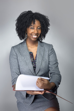 Black African American Businesswoman sitting and holding a folder of contracts or documents.  She looks like a secretary or a manager giving a business report. の写真素材