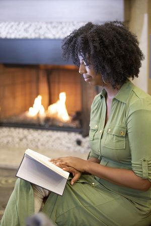 Black African American female resting at home and reading a book in a living room by a fireplace.  The woman is relaxing on a sofa in an apartment with a novel. の写真素材