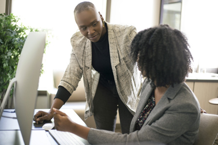 Black African American businesswomen or coworkers together in an office doing teamwork or job training.  The women are working together at a startup business.の写真素材