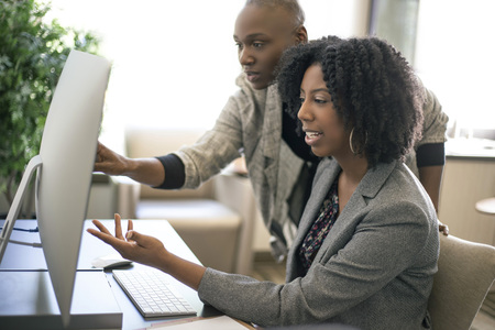 Black African American businesswomen or coworkers together in an office doing teamwork or job training.  The women are working together at a startup business.の写真素材