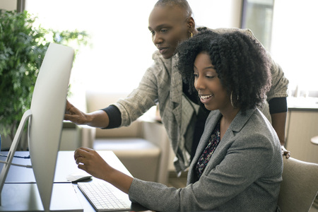 Black African American businesswomen or coworkers together in an office doing teamwork or job training.  The women are working together at a startup business.の写真素材