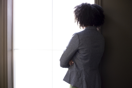 Silhouette of a stressed out black African American businesswoman looking worried and thinking about problems and failure by the office window.  She looks depressed or upset about debt or bankruptcy.の写真素材