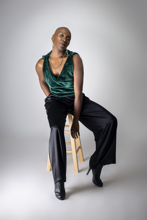 Black African American female fashion model wearing trendy green outfit and heels sitting on a stool.  She is confidently showing off a bold bald hairstyle.  の写真素材