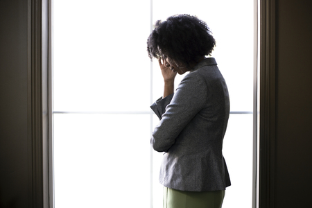 Silhouette of a stressed out black African American businesswoman looking worried and thinking about problems and failure by the office window.  She looks depressed or upset about debt or bankruptcy.の写真素材