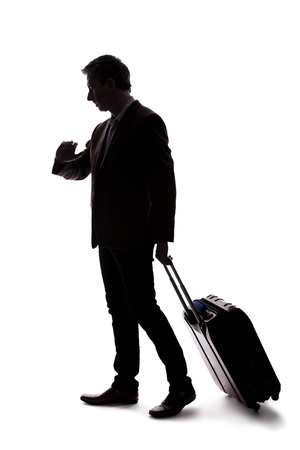 Silhouette of a traveling businessman looking upset because of a delayed or cancelled flight.  The traveler is stressed and waiting with his luggage.  Isolated on a white background.の写真素材