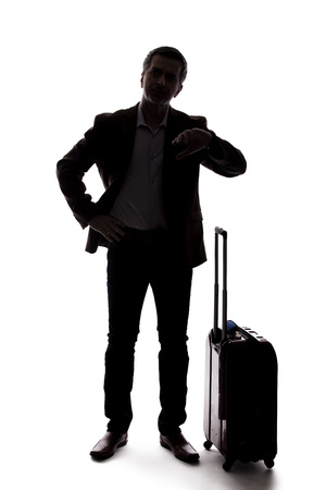 Silhouette of a traveling businessman looking upset because of a delayed or cancelled flight.  The traveler is stressed and waiting with his luggage.  Isolated on a white background.の写真素材