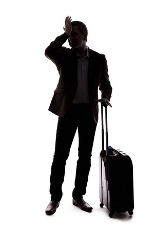 Silhouette of a traveling businessman looking upset because of a delayed or cancelled flight.  The traveler is stressed and waiting with his luggage.  Isolated on a white background.の写真素材