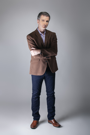 Bearded middle aged fashion model posing with business casual style outfit for mature and confident look.  The trendy brown jacket and jeans and facial hair shows an elegant apparel.の写真素材