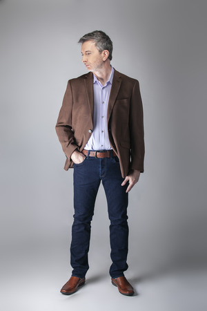 Bearded middle aged fashion model posing with business casual style outfit for mature and confident look.  The trendy brown jacket and jeans and facial hair shows an elegant apparel.の写真素材