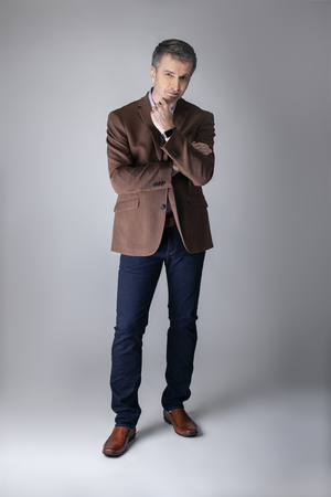 Bearded middle aged fashion model posing with business casual style outfit for mature and confident look.  The trendy brown jacket and jeans and facial hair shows an elegant apparel.の写真素材