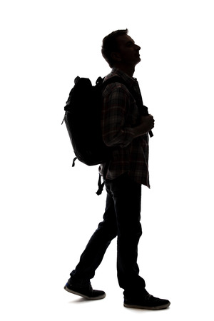 Silhouette of a male tour guide hiking and carrying a backpack on a white background.  The isolated side view man can be used for composites.  Depicts adventure and exploration.の写真素材