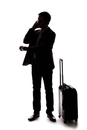 Silhouette of a businessman who is calling for a rideshare with a cellphone.  He is waiting with his luggage as if arriving from an airport.  Isolated on a white background for composites.の写真素材