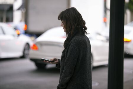 Female pedestrian waiting on a sidewalk for a rideshare.  She is sharing her gps location via...
