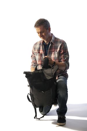 Middle-Aged tourist preparing a backpack for hiking or trekking during sunset.  He is isolated on white background for composites.の写真素材