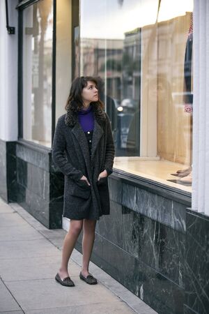 Woman walking outdoors in a city. She is window shopping and looking at a store sale advertising or marketing apparel and clothing on a display glass. の写真素材