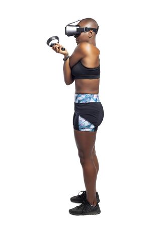 Black female wearing a virtual reality headset and holding wand controllers doing vr fitness exercises.  The gamer is in a sports simulation video game for entertainment and healthy physical activity.の写真素材