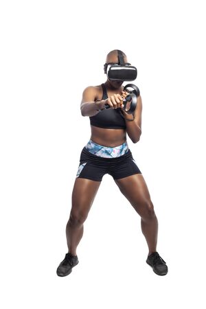 Athletic black female gamer playing video games and exercising while wearing a virtual reality headset.  She is punching like she is boxing or fighting.  Depicts wearable technology and healthy activities.の写真素材