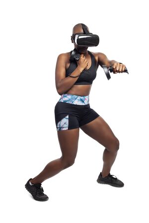 Athletic black female gamer playing video games and exercising while wearing a virtual reality headset.  She is punching like she is boxing or fighting.  Depicts wearable technology and healthy activities.の写真素材