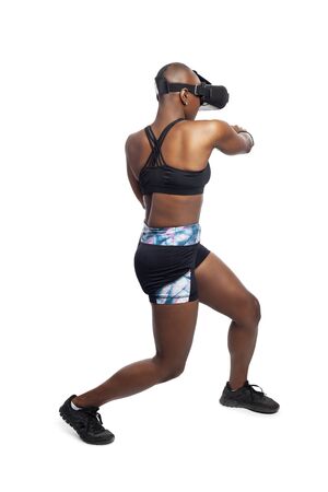 Athletic black female gamer playing video games and exercising while wearing a virtual reality headset.  She is punching like she is boxing or fighting.  Depicts wearable technology and healthy activities.の写真素材