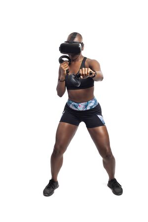 Athletic black female gamer playing video games and exercising while wearing a virtual reality headset.  She is punching like she is boxing or fighting.  Depicts wearable technology and healthy activities.の写真素材