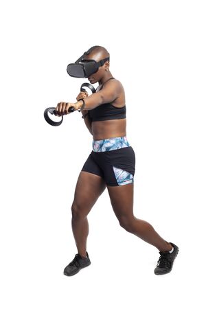 Athletic black female gamer playing video games and exercising while wearing a virtual reality headset.  She is punching like she is boxing or fighting.  Depicts wearable technology and healthy activities.の写真素材