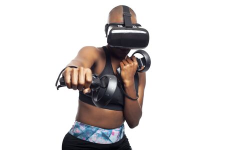 Athletic black female gamer playing video games and exercising while wearing a virtual reality headset.  She is punching like she is boxing or fighting.  Depicts wearable technology and healthy activities.の写真素材