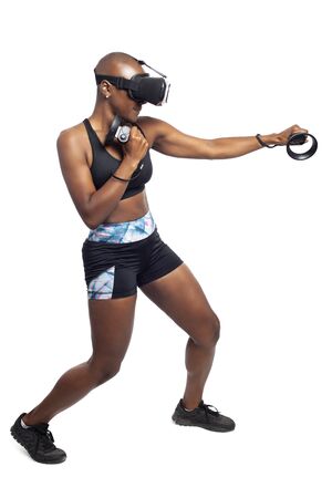 Athletic black female gamer playing video games and exercising while wearing a virtual reality headset.  She is punching like she is boxing or fighting.  Depicts wearable technology and healthy activities.の写真素材