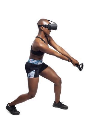Athletic woman exercising while playing video game by practicing VR sword fighting or swordplay with a virtual reality headset and controller. Depicts healthy active gaming for fitness.の写真素材