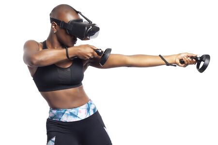 Athletic black female playing a first person shooter video game in VR with a virtual reality headset and controllers. She is pretending to shoot a gun or rifle. Depicts gaming and exercise.の写真素材