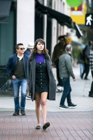Young pretty female millennial walking on foot in the city and crossing a paved pedestrian cross walk.  She is either a commuter or a tourist who is exploring and sightseeing.の写真素材