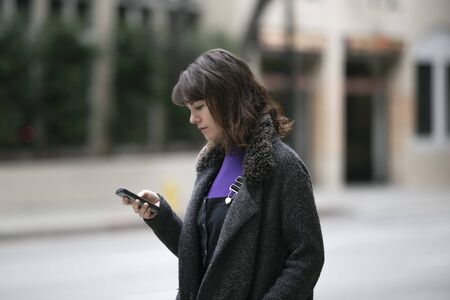 Young female using mobile phone app and waiting for a rideshare or pedestrian tourist checking online map for gps navigation.  Depicts city life and how millennials travel.の写真素材