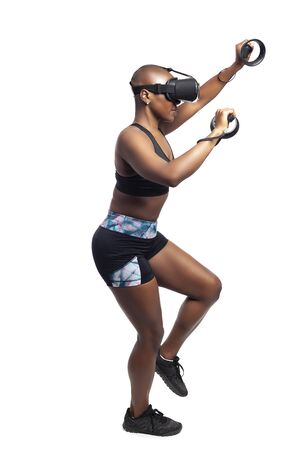 Athletic black female playing a vr video game pretending to do mountain climbing in virtual reality.  She is gaming while exercising to depict technology and healthy activities.の写真素材