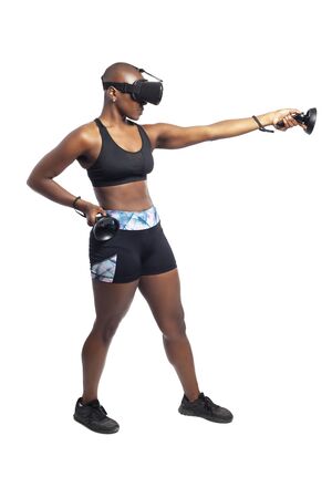 Athletic black female playing a first person shooter video game in VR with a virtual reality headset and controllers. She is pretending to shoot a gun or rifle. Depicts gaming and exercise.の写真素材