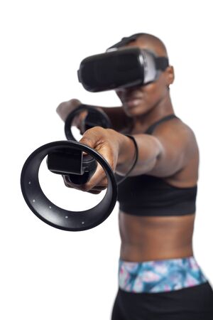 Black female gamer holding virtual reality controllers or wands and wearing a VR headset.  She is playing an interactive video game.  Depicts 3d technology.の写真素材