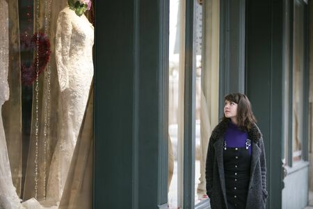 Caucasian female walking in the city and window shopping for a wedding dress.  She is either making decisions for wedding plans or a single woman aspiring to be a bride.の写真素材