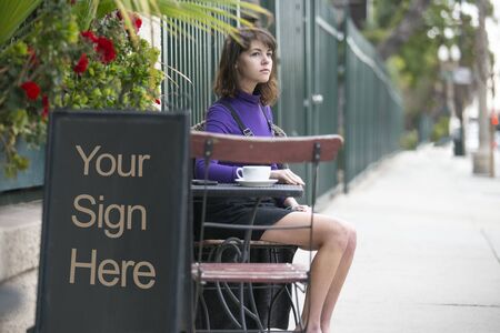 Empy blank sign board in front of a restaurant cafe or coffee shop with a female customer sitting down and waiting.  The image has copy space for logos or text. Depicts advertising and marketing.の写真素材