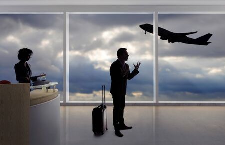 Stressed out businessman passenger arguing with a flight attendant or receptionist at an airport check in counter.  He is angry because of a delayed or cancelled flight.の写真素材