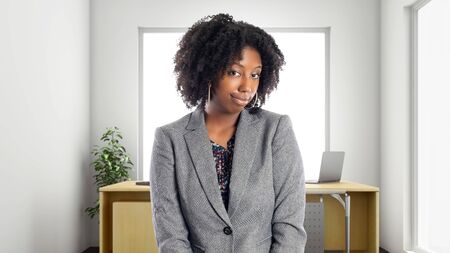 Black African American businesswoman in an office looking shy.  She is an owner or an executive of the workplace.  Depicts careers and startup business.の写真素材