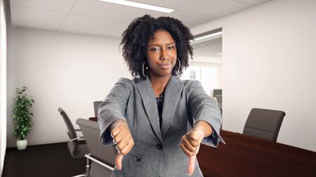 Black African American businesswoman in an office with thumbs down.  She is an owner or an executive of the workplace.  Depicts careers and startup business.の写真素材