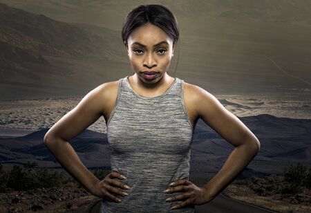Athletic black African American female runner or jogger resting to pose with a motivated facial expression with a road during sunset in the background.  Depicts endurance and determination during marathon sports.の写真素材