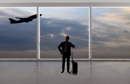 Silhouette of a traveling businessman with luggage in front of an airport window with a view of the sky and an airplane.  The panorama has copy space for text.  Depicts business travel.の写真素材