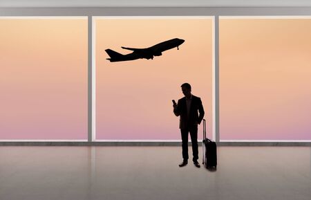 Silhouette of a traveling businessman with luggage in front of an airport window with a view of the sky and an airplane.  The panorama has copy space for text.  Depicts business travel.の写真素材