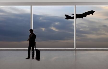 Silhouette of a traveling businessman with luggage in front of an airport window with a view of the sky and an airplane.  The panorama has copy space for text.  Depicts business travel.の写真素材