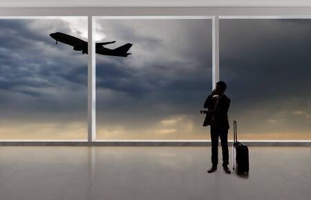 Silhouette of a traveling businessman with luggage in front of an airport window with a view of the sky and an airplane.  The panorama has copy space for text.  Depicts business travel.の写真素材
