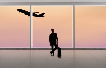 Silhouette of a traveling businessman with luggage in front of an airport window with a view of the sky and an airplane.  The panorama has copy space for text.  Depicts business travel.の写真素材