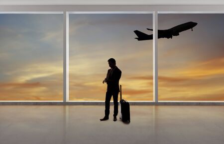 Silhouette of a traveling businessman with luggage in front of an airport window with a view of the sky and an airplane.  The panorama has copy space for text.  Depicts business travel.の写真素材